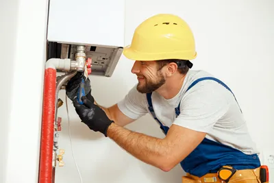 A heating engineer working on the pipes under a boiler.